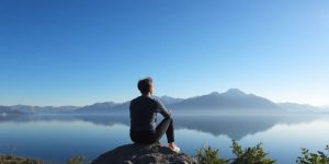 Person reflecting by a calm lake in a natural setting.